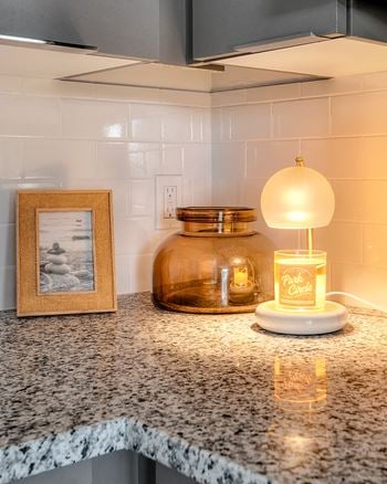 A picture frame, a glass container, and a lit candle are on a granite countertop.